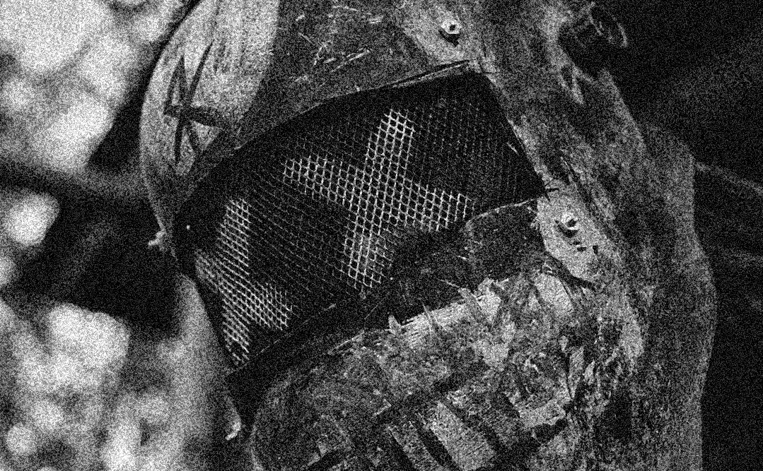 Close-up black-and-white photo of a weathered raider helmet with a mesh visor and a scratched mark on the side.